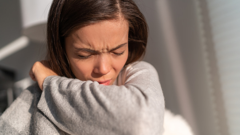 A woman sneezes into her elbow