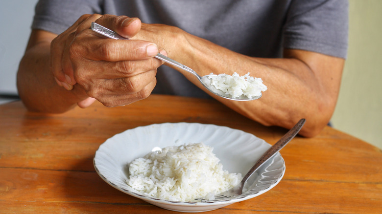 Man eating rice with a spoon, holding his wrist