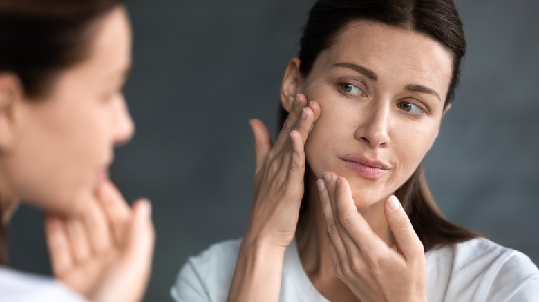 A concerned looking middle-aged woman checking her skin 