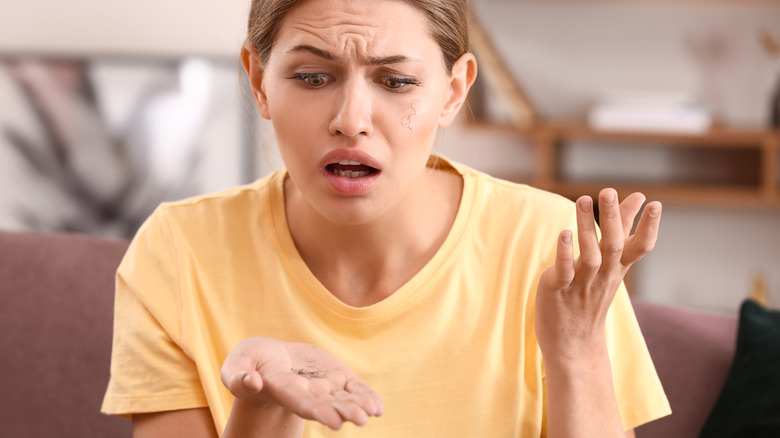 confused young woman looking at her shedding eyebrow hair 