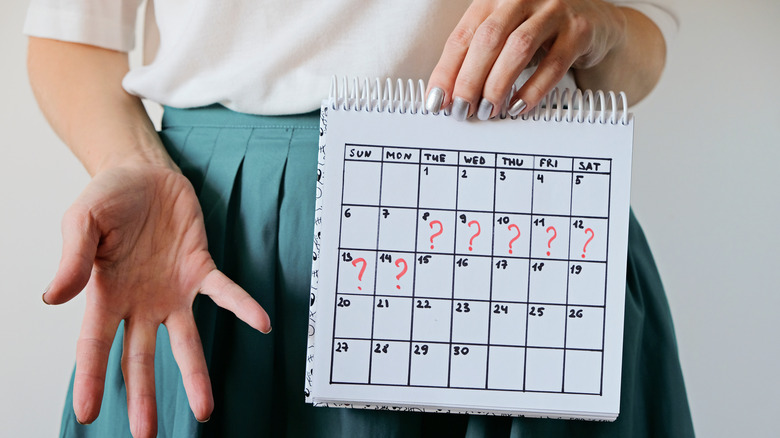 Confused woman holding a calendar with question marks