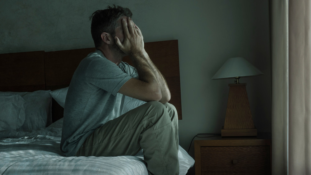 Man sitting on the edge of his bed with his face in his hands