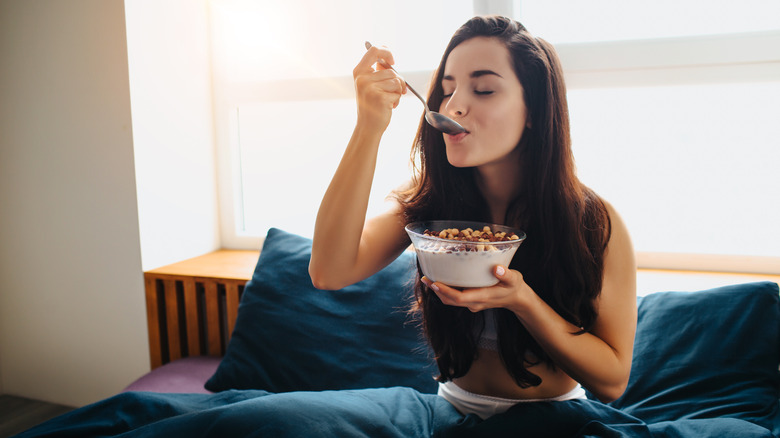 A woman eats cereal in bed