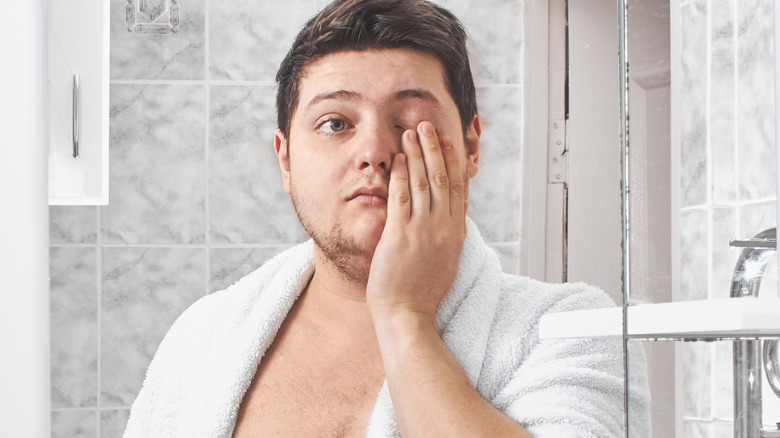 Man in mirror holding one eye shut