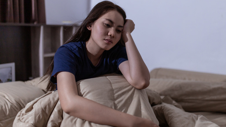 Woman sitting up in bed with hand on head 