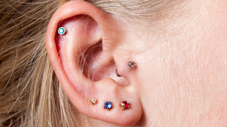 Close-up of woman's ear with multiple colorful earring studs