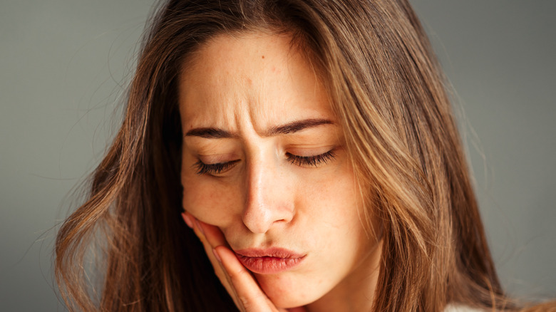 Close-up portrait of a young girl in a white shirt holding her jaw in pain
