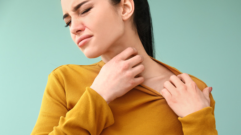 Woman wincing and pulling on her yellow sweater and scratching her neck