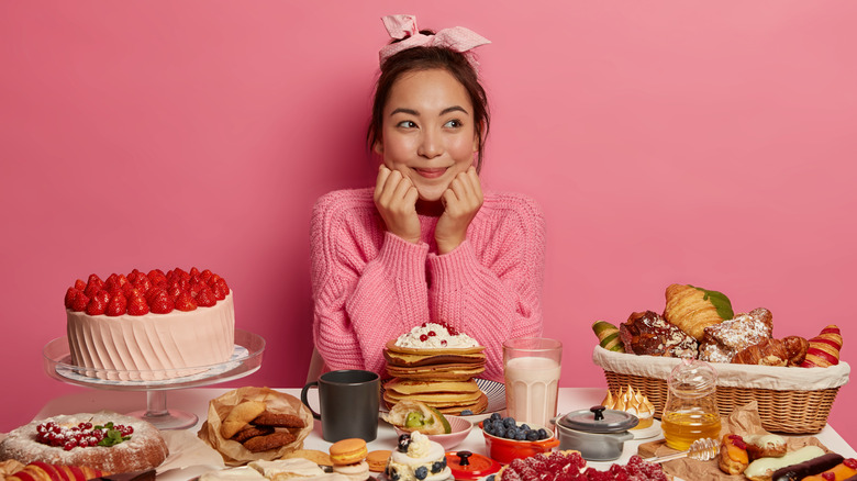 smiling woman behind a table of sweets with an all pink background 