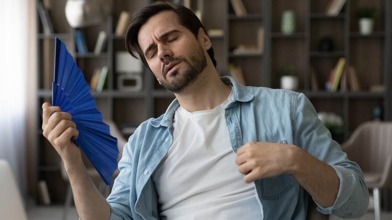 Man feeling uncomfortably warm fanning himself in front of his laptop 