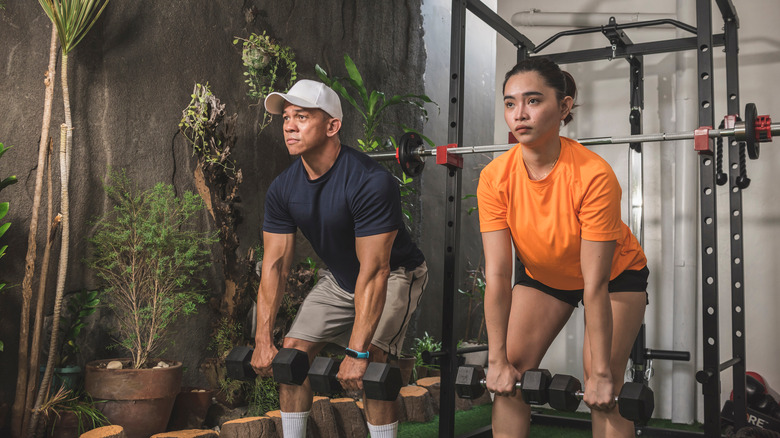 Two people practice deadlifts with dumbbells 