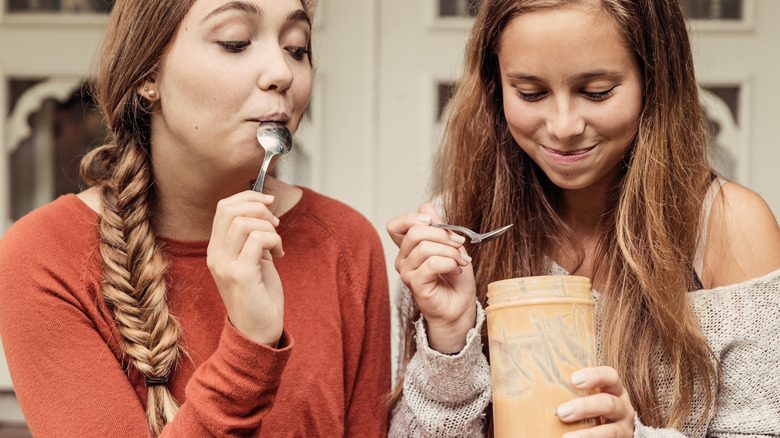two women eating peanut butter from a jar