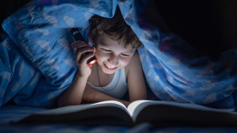 Child using flashlight to read in bed