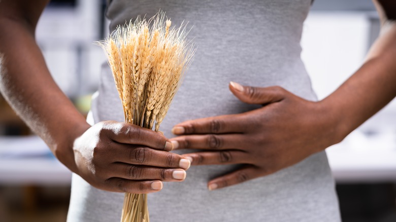Woman holding wheat shafts and other hand to stomach