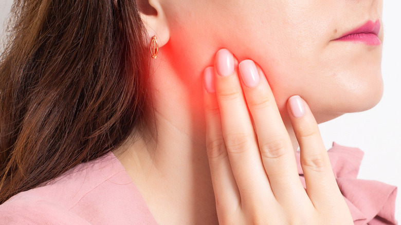 Close up of woman in pink shirt touching her inflamed jaw