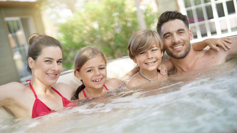 Family of four soaking in a hot tub and smiling 