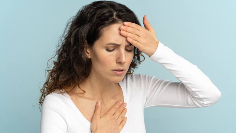 A woman looks uncomfortable with her hand on her forehead and her chest