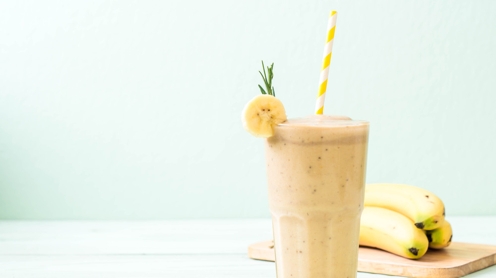 Banana smoothie in glass with straw and bananas in background