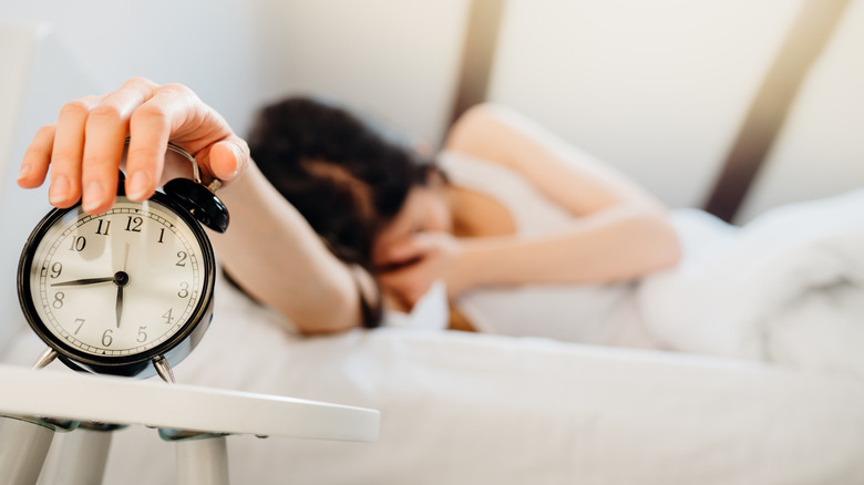 woman in bed pressing snooze on alarm clock