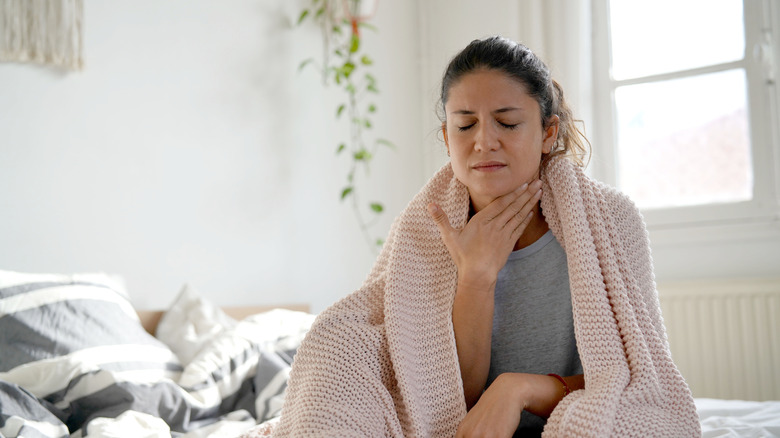 Woman sits on bed with a sore throat