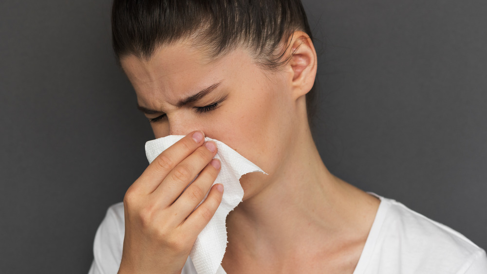 woman suffering from an illness, blowing her nose in a tissue 