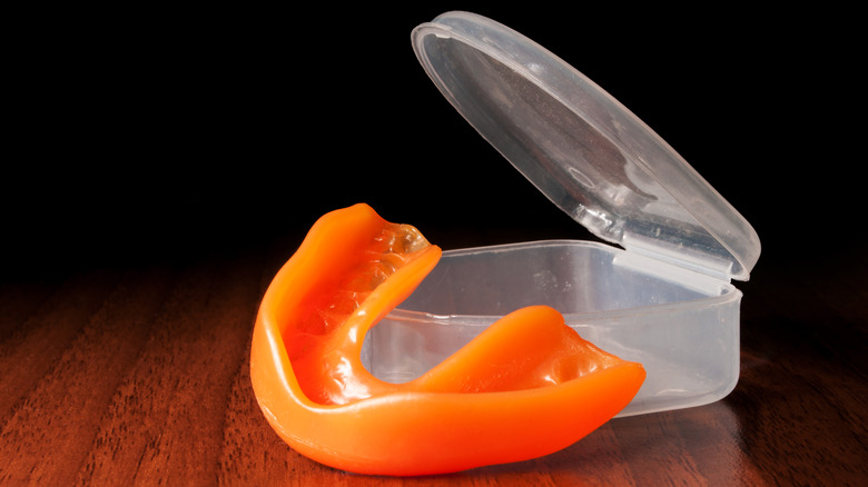 Orange mouth guard resting on open case on wooden table against black background