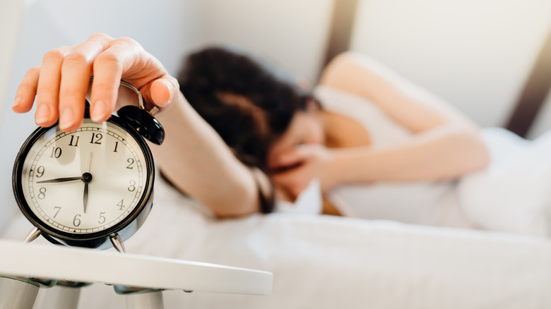 Woman in bed turning off her alarm clock