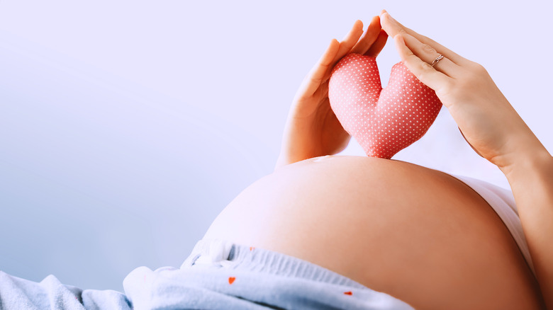 Close up of a pregnant woman's hands holding a heart over her belly