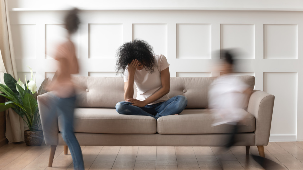 A mom holding her head with a migraine as blurred children run around