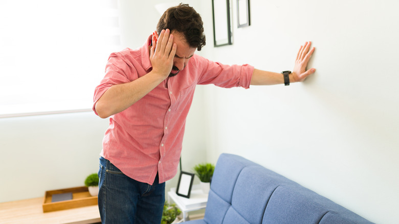 man feeling dizzy and holding onto a wall