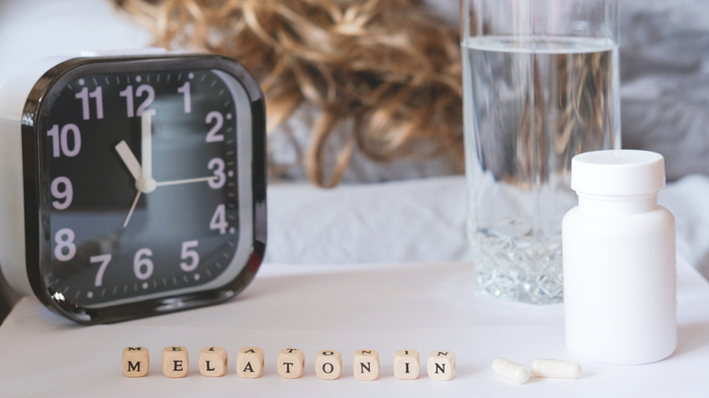 an alarm clock, glass of water, pill bottle, and the word "melatonin" spelled out on the night table 