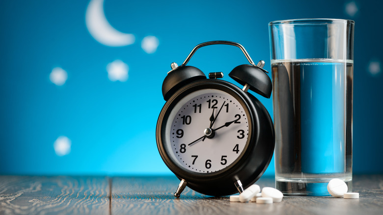 pills, glass of water, and alarm clock with nighttime background