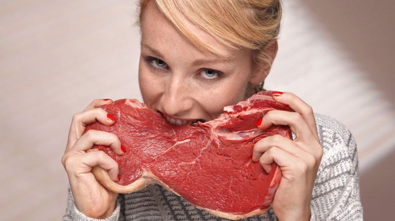 A woman biting into a piece of raw meat