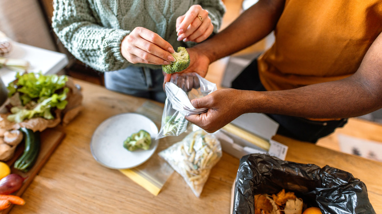 two people putting broccoli into a plastic bag