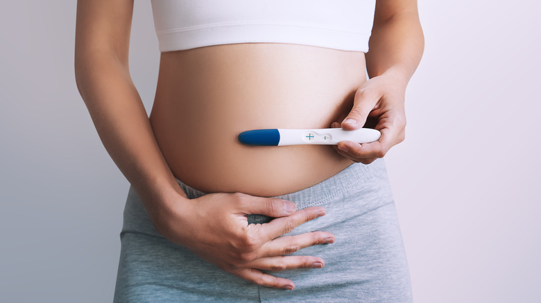 woman holding pregnancy test to belly 
