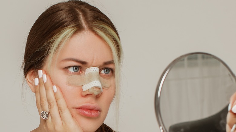 Woman looking in mirror after rhinoplasty