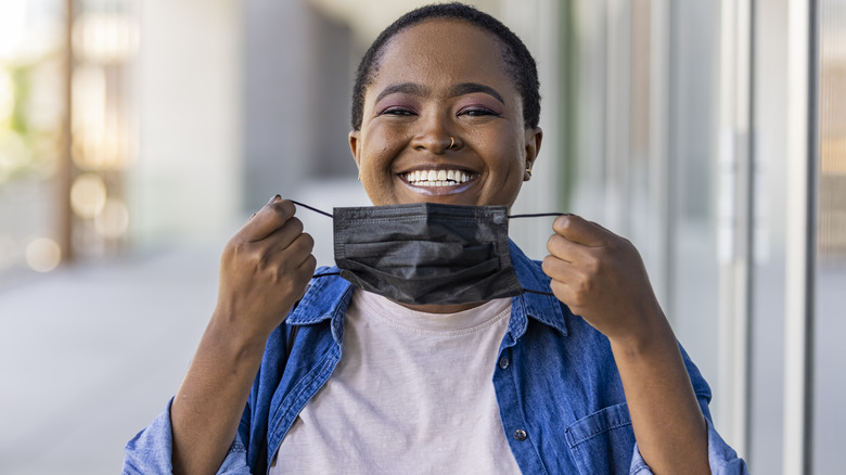 Smiling young woman removing face mask