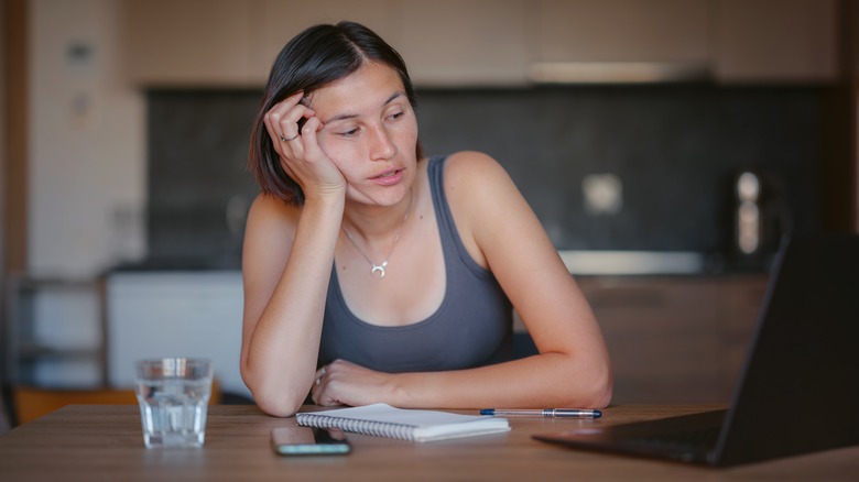 A tired woman looks at her laptop