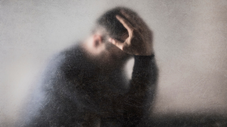 Man with head hanging low, holding his head in his hands