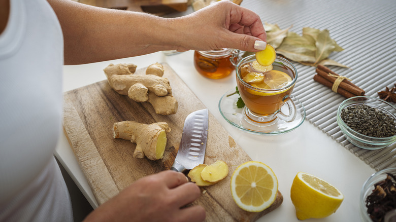 A woman's hand adding sliced ginger to hot tea