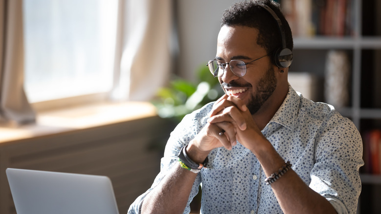 Man smiling while wearing headphones and working on laptop