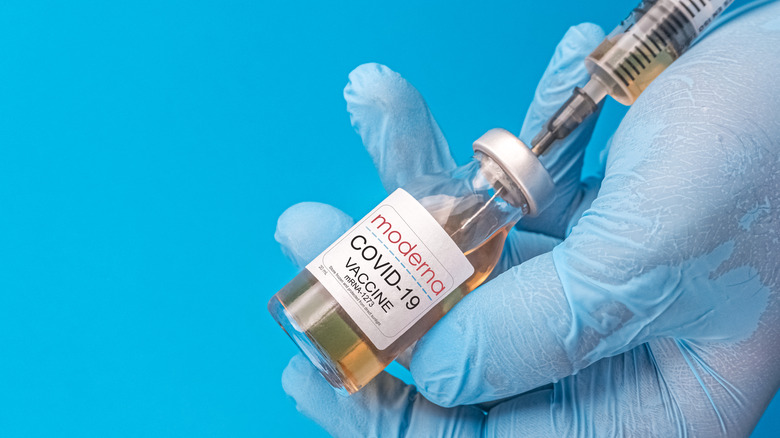 Close up of vial of Moderna COVID-19 vaccine with syringe in hands wearing blue gloves