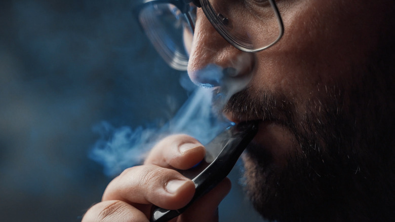 Man in glasses smoking e-cigarette surrounded by smoke