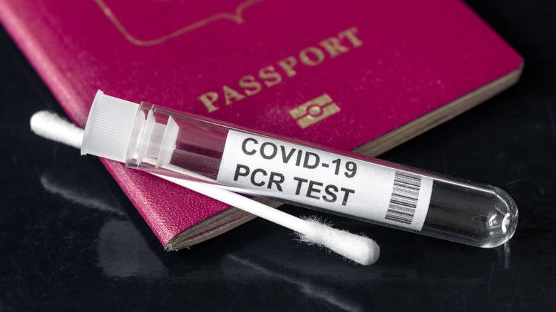 COVID-19 PCR test tube laying next to a q-tip and red passport on a black table