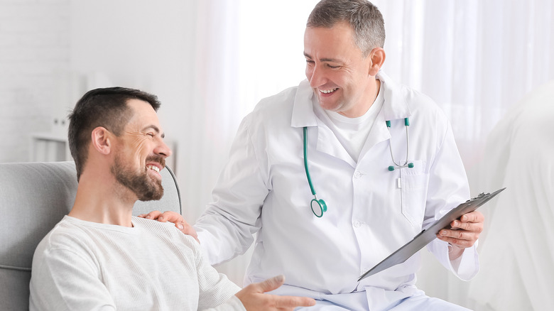 Doctor in white lab coat holding a clipboard talking to a male patient