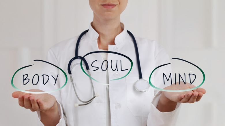 A doctor holding out her hands. The words "body", "soul", and "mind" are balanced between her hands