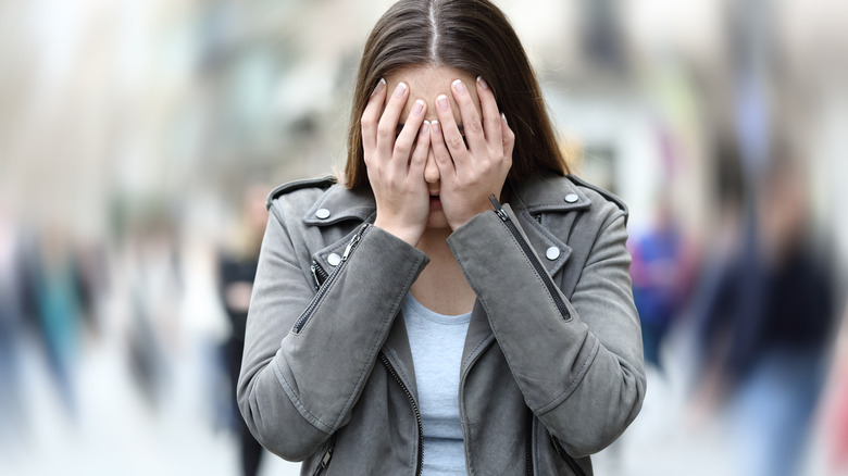 A woman suffering from anxiety on city street with her face in her hands