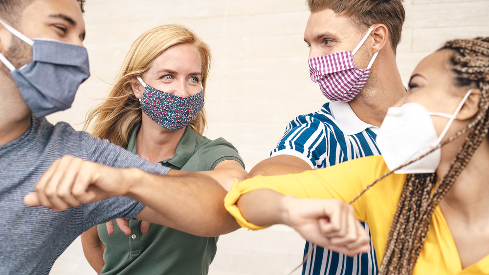 Friends with face masks saying hello with elbows