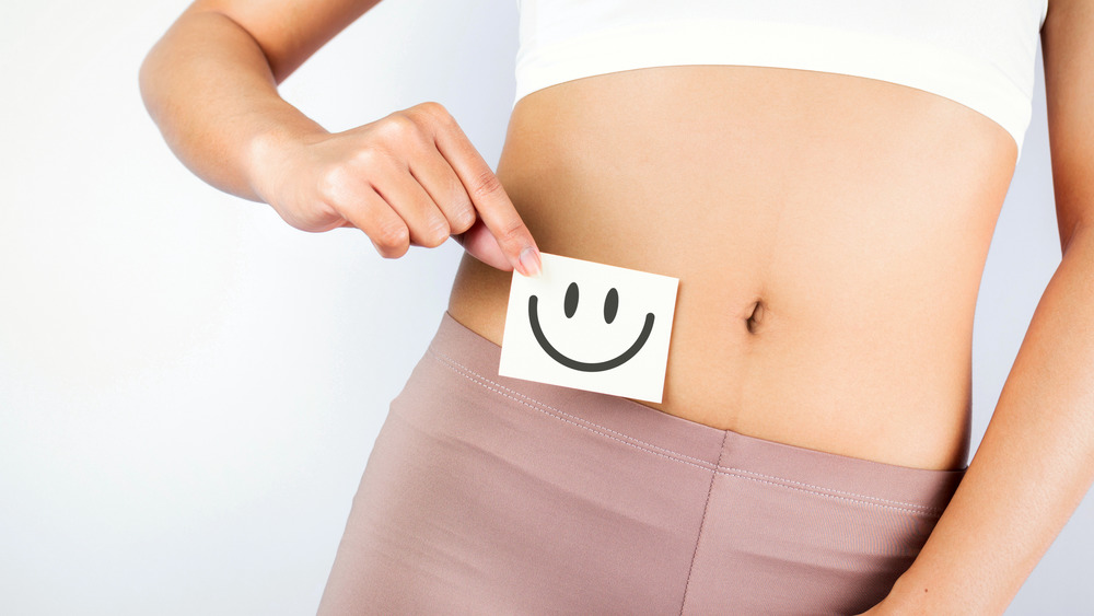 A woman holding up a post-it with a smiley face next to her bare midriff 