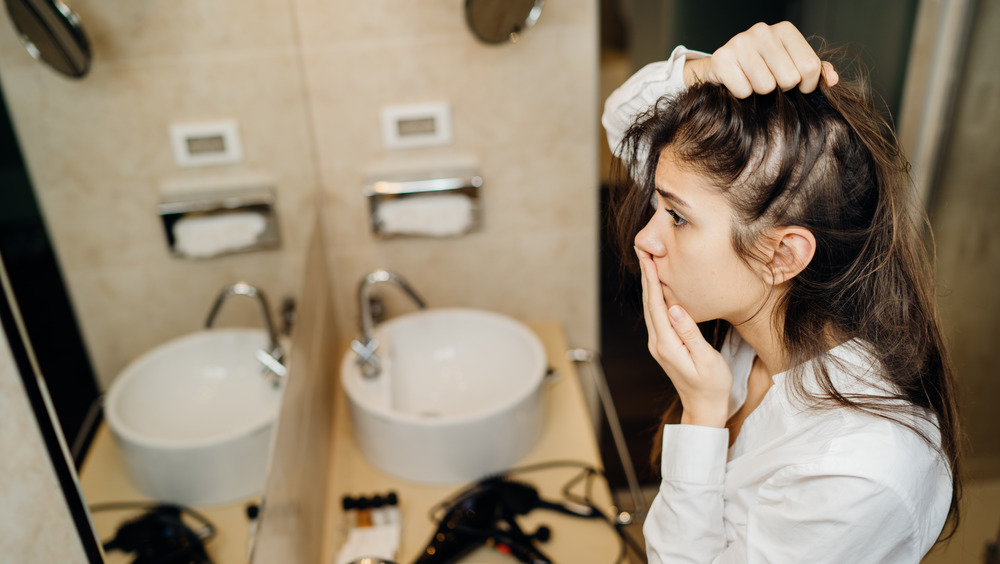 Worried woman looking at hair in mirror